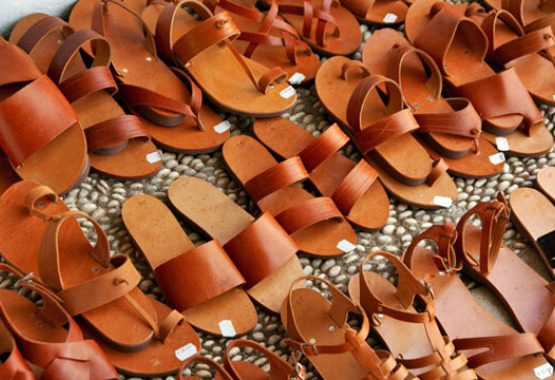 Three rows of leather sandals on paved surface with white pebbles.