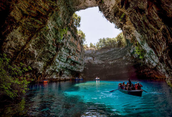 Σπήλαιο με γαλαζοπράσινα νερά και άνοιγμα στην κορυφή που φαίνεται ο ουρανός και δέντρα. Βάρκες με ανθρώπους πάνω στο νερό.