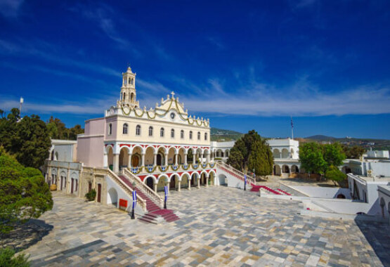 Large church with arches and stairs in a paved courtyard surrounded by trees and other buildings.