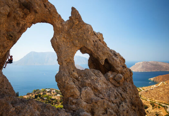 Απότομος βράχος με 2 μεγάλες τρύπες. Πίσω τους φαίνεται στεριά, θάλασσα και νησιά. Άντρας σκαρφαλώνει στην μεγαλύτερη τρύπα.