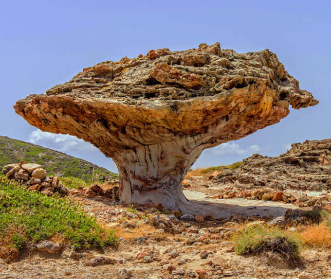 Mushroom-shaped rock in a rocky landscape with low green vegetation. 