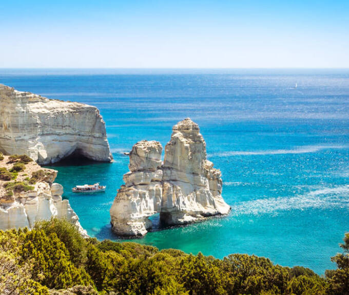 High cliffs above the sea with bushes. Typical large rock with a hole in the sea and next to a small boat. 