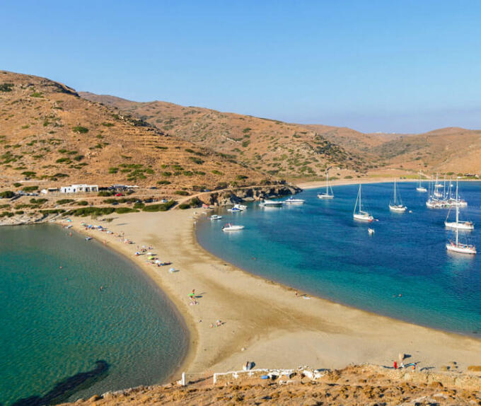 Thin strip of land that forms 2 beaches. Many sailing boats on one. Gentle hills with few buildings. 