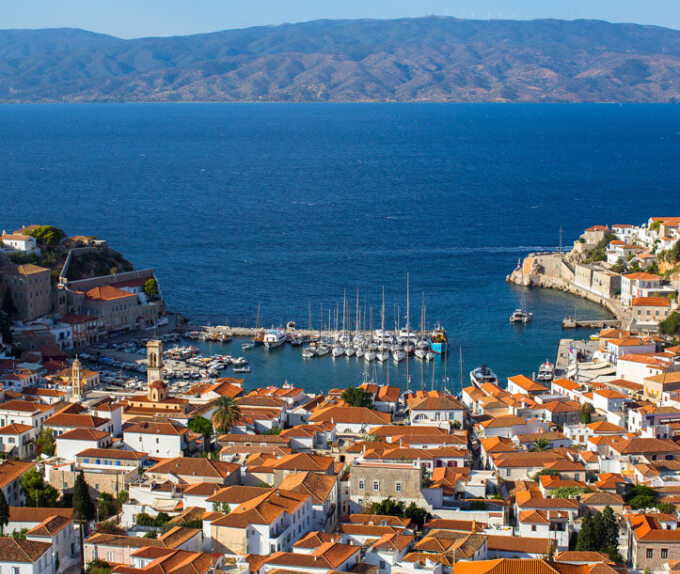 View from above of a small bay with small boats surrounded by a traditional settlement with red roofs. 