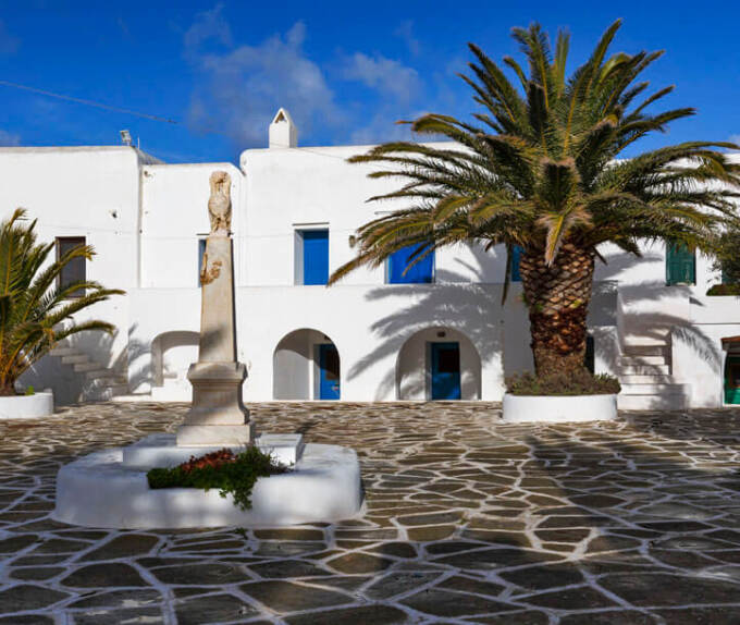 Paved square with a column, palm tree and white houses with arches. 