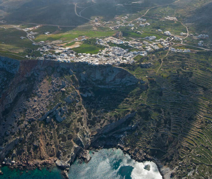 Aerial view of a settlement on a high cliff above the sea with green areas around. 