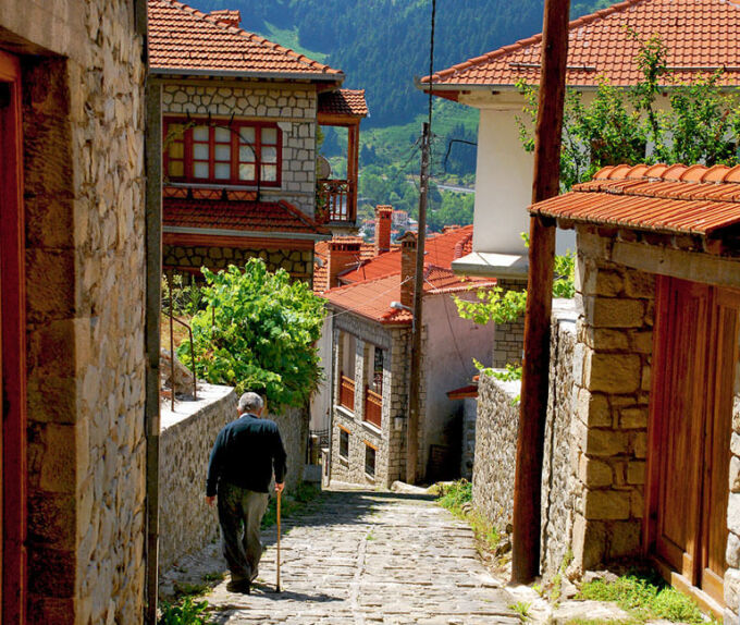 Old man walking down a cobblestone alley lined with stonebuilt houses on a sunny winter day in Metsovo