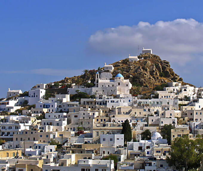 White houses densely built on the slope of a small hill. At the top 3 small churches. 