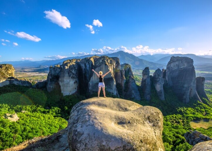 back of a woman with her arms in the air, overlooking the meteora rocks