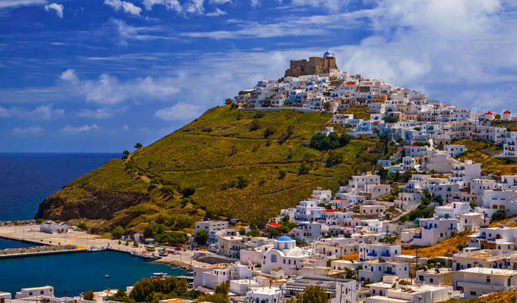 Λόφος με κάστρο στην κορυφή και οικισμό με άσπρα σπίτια που καταλήγει σε μικρό λιμάνι.