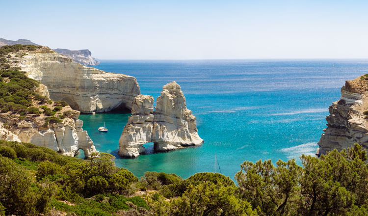 High cliffs above the sea with bushes. Typical large rock with a hole in the sea and next to a small boat. 