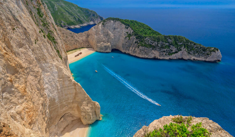 Zakynthos beach with white sand and the greenish blue waters between the steep rocks, with a boat that has shipwrecked on the beach