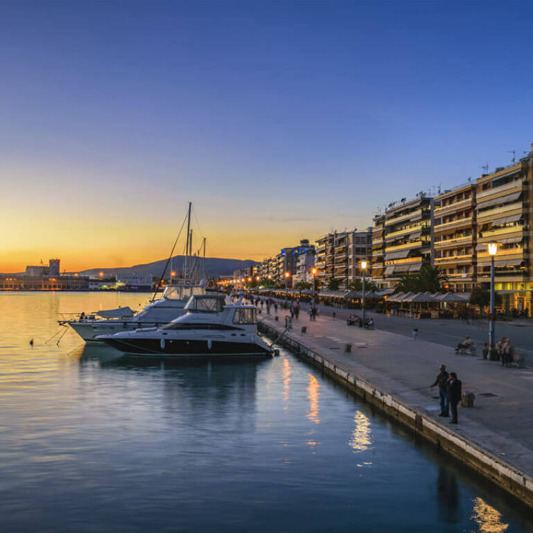 Waterfront with yachts and pedestrian street with people. Apartment buildings with restaurants downstairs. 