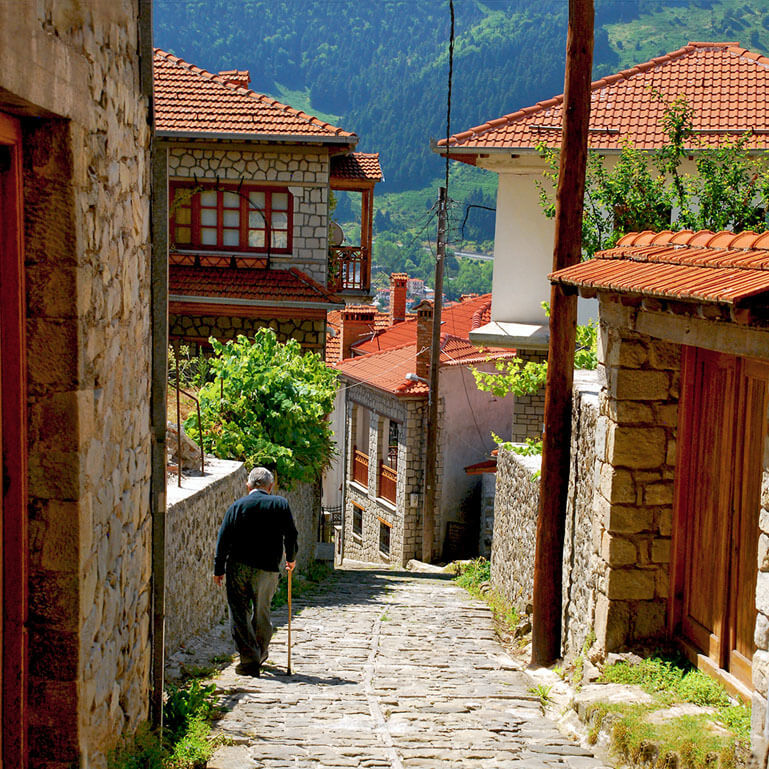 Old man walking down a cobblestone alley lined with stonebuilt houses on a sunny winter day in Metsovo