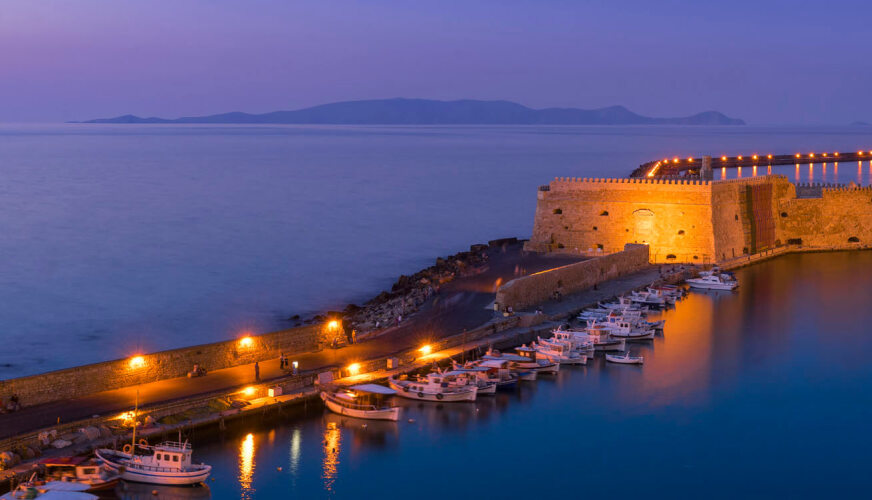 Προβλήτα με βάρκες και μικρό πέτρινο κάστρο το δειλινό με αναμμένα τα φώτα.