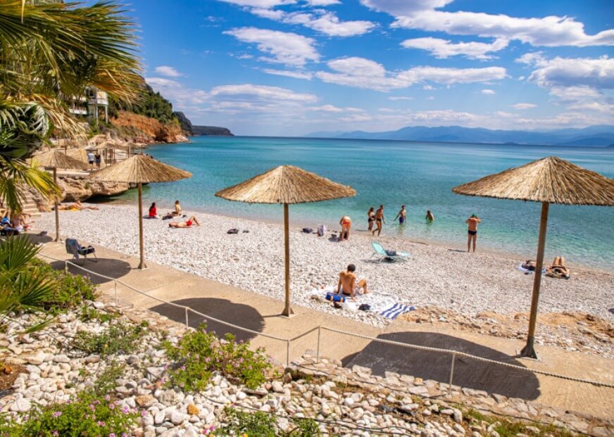 people and beach umbrellas on pebbly Arvanitia beach 